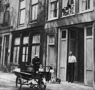 876893 Afbeelding van een man staande voor zijn pakhuis aan de Waterstraat in Wijk C te Utrecht, met op straat een ...